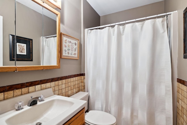 bathroom featuring toilet, a shower with shower curtain, vanity, tile walls, and wainscoting