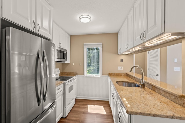 kitchen with dark wood-style flooring, appliances with stainless steel finishes, a sink, a wainscoted wall, and a peninsula