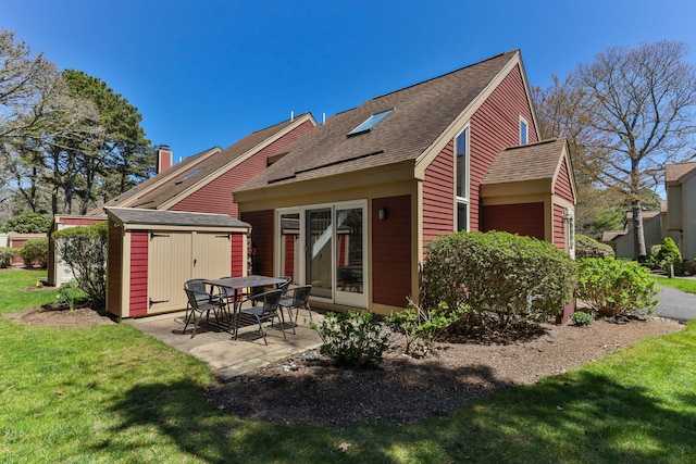 back of property featuring a lawn, an outbuilding, a patio area, a shed, and a shingled roof