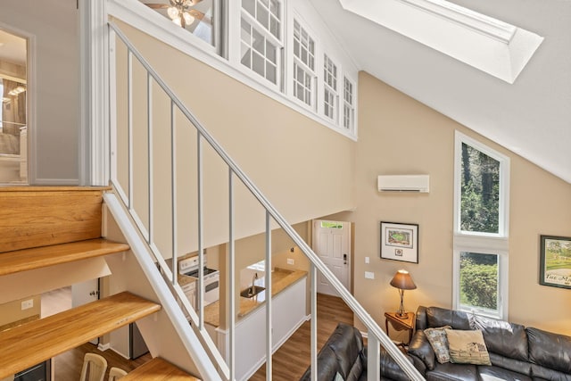 staircase with a wall unit AC, lofted ceiling with skylight, and wood finished floors