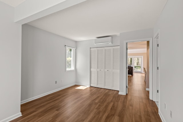 unfurnished bedroom with wood finished floors, baseboards, a wall mounted AC, and a closet