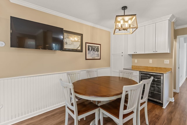 dining space with crown molding, an inviting chandelier, wine cooler, dark wood-style floors, and a wainscoted wall