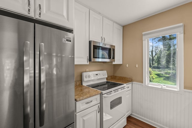 kitchen featuring white cabinetry, appliances with stainless steel finishes, wainscoting, and a wealth of natural light