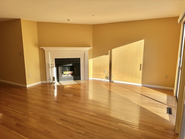 unfurnished living room with baseboards, visible vents, wood finished floors, and a fireplace with flush hearth