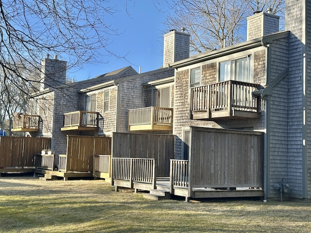 back of property featuring a deck, a chimney, and a lawn