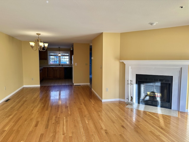 unfurnished living room featuring a fireplace with flush hearth, visible vents, light wood-style flooring, and a notable chandelier