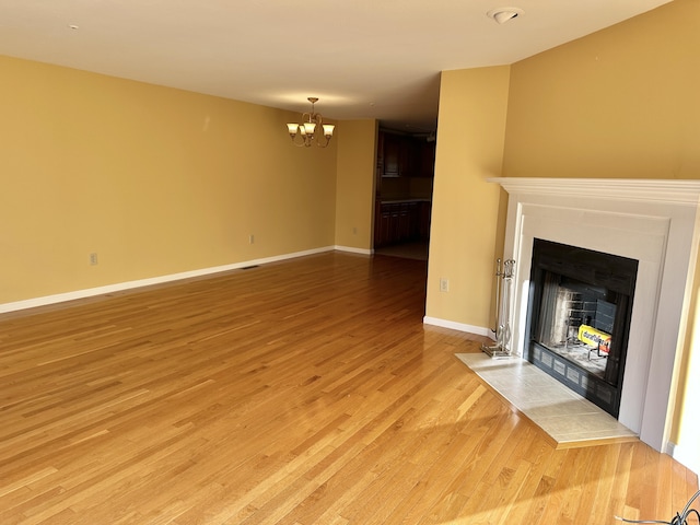 unfurnished living room featuring a chandelier, a fireplace, light wood-style flooring, and baseboards