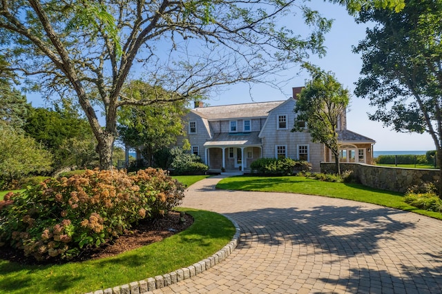 shingle-style home with a front lawn, a chimney, fence, and a gambrel roof