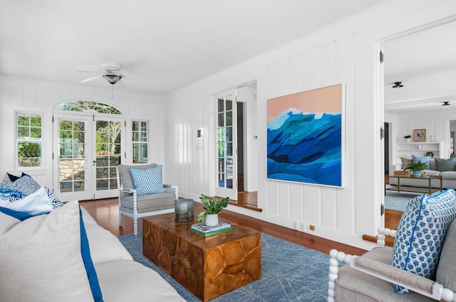 living area with french doors, a decorative wall, ornamental molding, ceiling fan, and wood finished floors