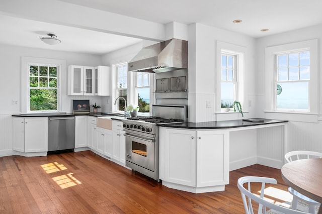 kitchen featuring hardwood / wood-style floors, appliances with stainless steel finishes, wall chimney range hood, white cabinets, and sink