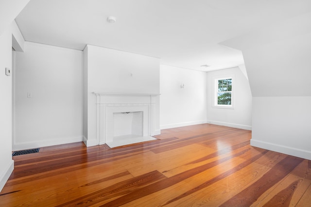 unfurnished living room with wood finished floors, a fireplace with flush hearth, visible vents, and baseboards