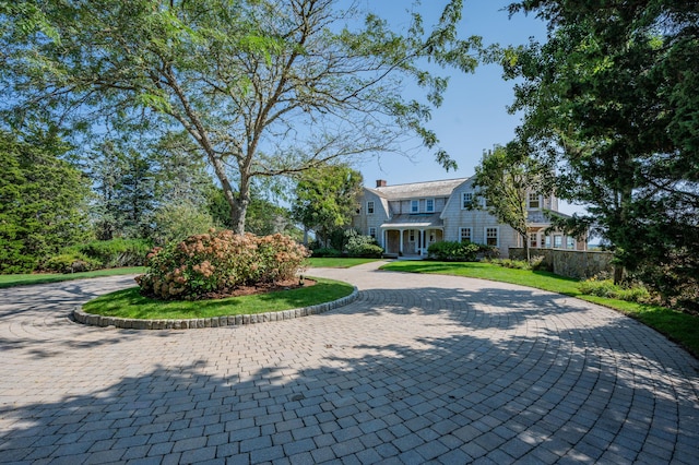 view of front facade featuring a front lawn, decorative driveway, and a gambrel roof