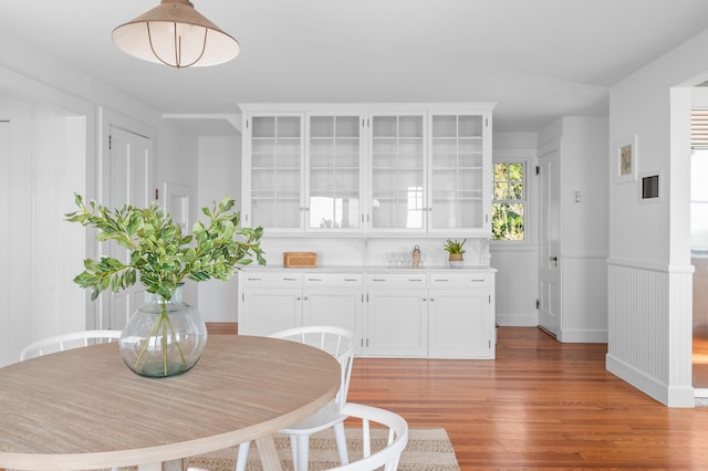 kitchen with a wainscoted wall, glass insert cabinets, light countertops, light wood-style floors, and white cabinetry