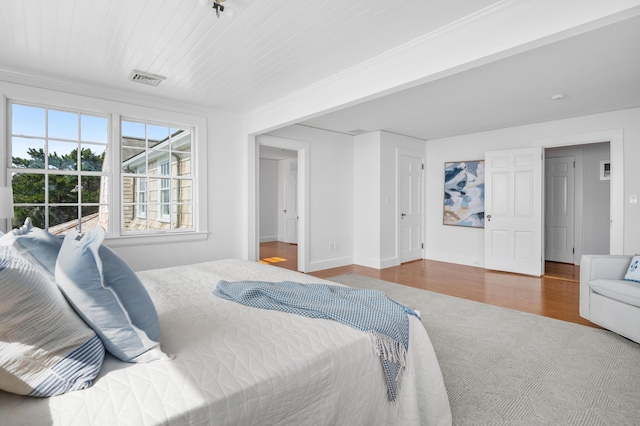 bedroom with ornamental molding, visible vents, baseboards, and wood finished floors