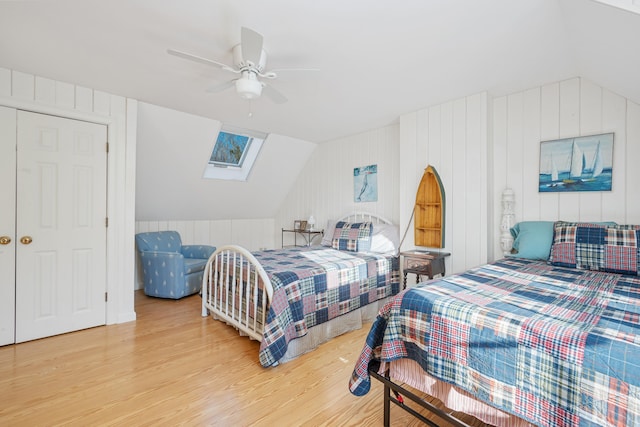 bedroom with ceiling fan, light hardwood / wood-style floors, and vaulted ceiling with skylight