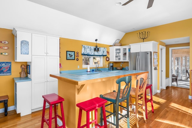 kitchen with vaulted ceiling, tile countertops, stainless steel fridge, white cabinets, and a kitchen bar