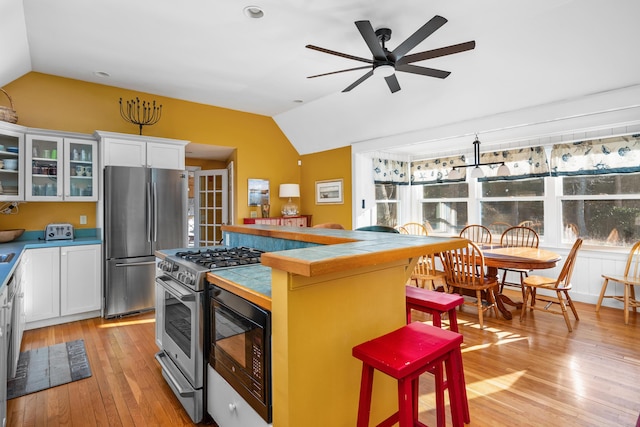 kitchen with vaulted ceiling, appliances with stainless steel finishes, white cabinets, and light wood-type flooring