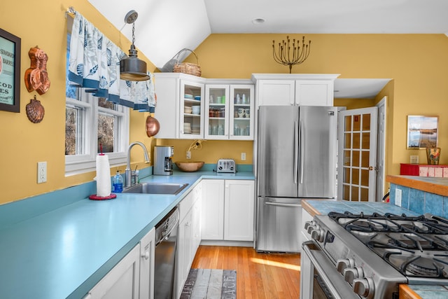 kitchen with decorative light fixtures, sink, white cabinets, stainless steel appliances, and light wood-type flooring