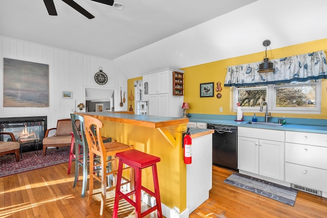 kitchen with sink, a kitchen breakfast bar, black dishwasher, pendant lighting, and white cabinets