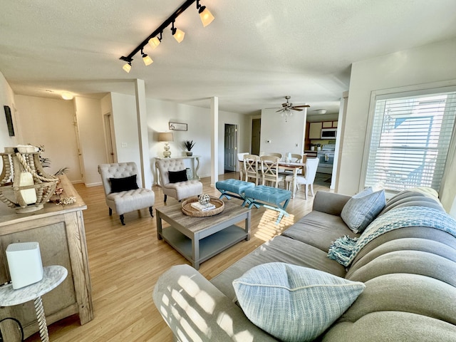 living room featuring ceiling fan, light hardwood / wood-style flooring, rail lighting, and a textured ceiling