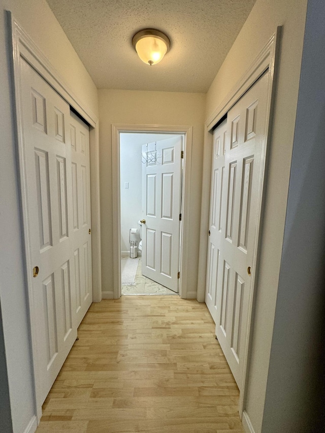 corridor with a textured ceiling and light wood-type flooring