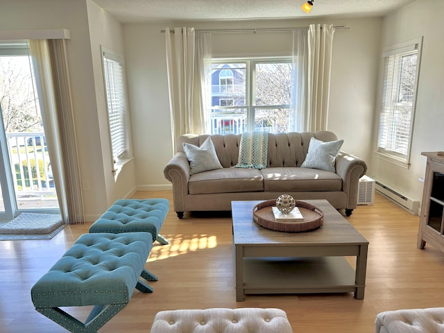 living room with light hardwood / wood-style flooring, a healthy amount of sunlight, a baseboard heating unit, and a textured ceiling