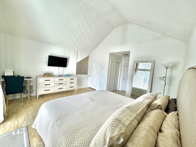 bedroom featuring light hardwood / wood-style floors, a textured ceiling, and lofted ceiling