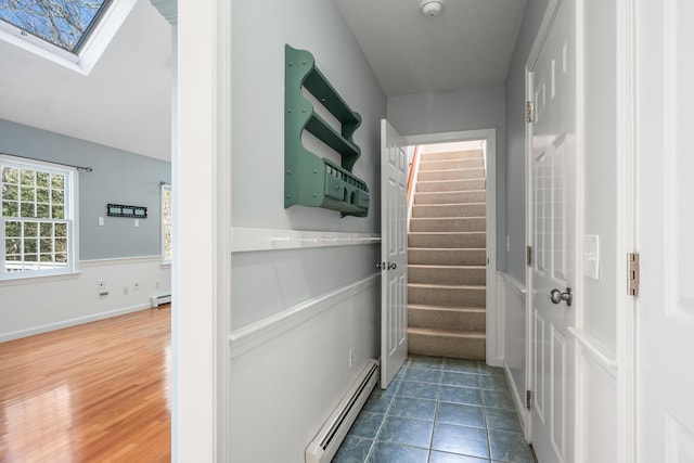 hallway with stairs, a baseboard radiator, tile patterned floors, and a skylight