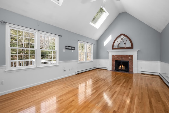 unfurnished living room featuring wainscoting, baseboard heating, a brick fireplace, and light wood-style floors