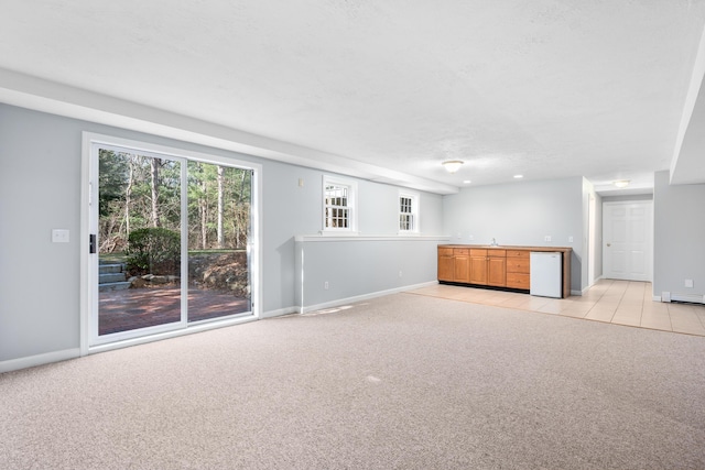 unfurnished living room featuring plenty of natural light, light colored carpet, a sink, and baseboards