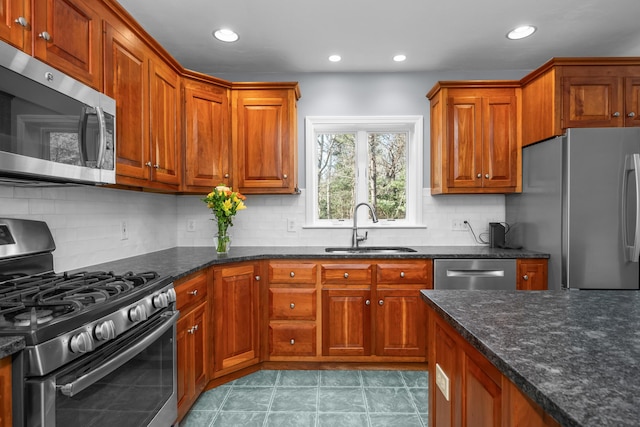 kitchen featuring light tile patterned floors, stainless steel appliances, brown cabinetry, and a sink