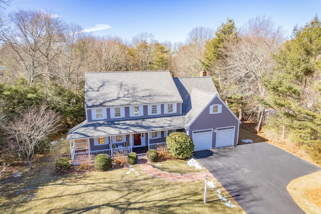 view of front of home with driveway, a garage, a chimney, a porch, and a front lawn