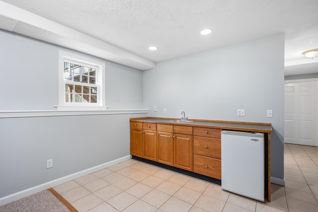 kitchen with brown cabinets, light tile patterned floors, a sink, baseboards, and fridge