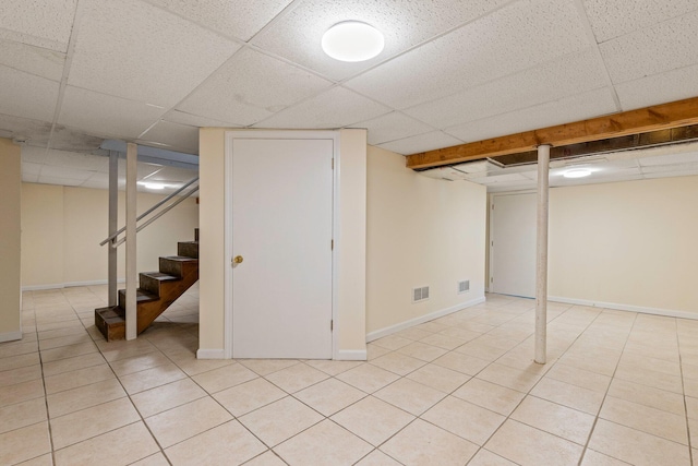 finished basement with light tile patterned floors, visible vents, stairs, and a paneled ceiling