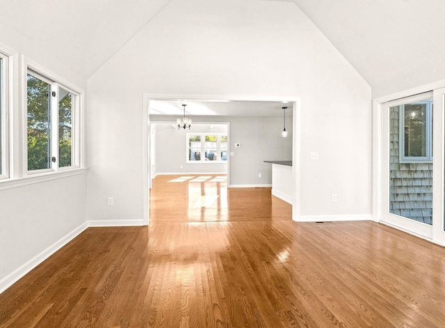 unfurnished room with high vaulted ceiling, baseboards, a notable chandelier, and wood finished floors