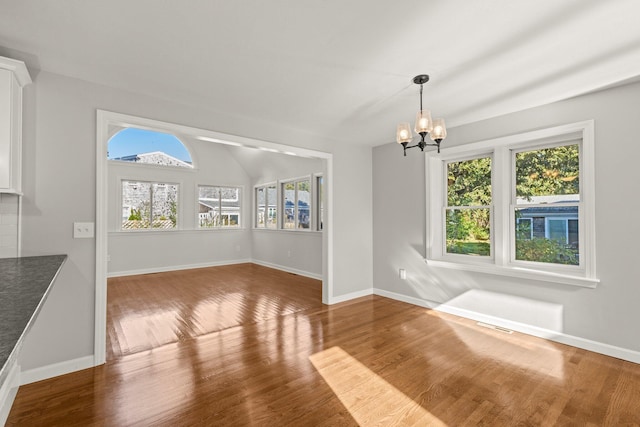 unfurnished dining area with a chandelier, wood finished floors, visible vents, baseboards, and vaulted ceiling