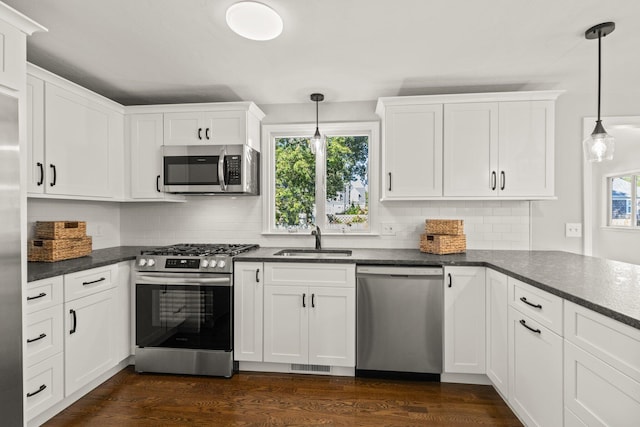 kitchen featuring white cabinets, dark countertops, appliances with stainless steel finishes, pendant lighting, and a sink