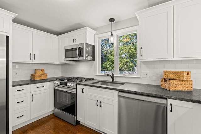 kitchen with stainless steel appliances, dark countertops, a sink, and white cabinetry