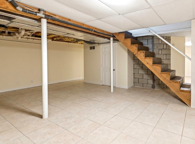 finished basement featuring light tile patterned floors, visible vents, baseboards, stairs, and a paneled ceiling