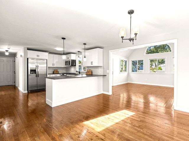 kitchen with pendant lighting, dark countertops, appliances with stainless steel finishes, white cabinets, and a peninsula