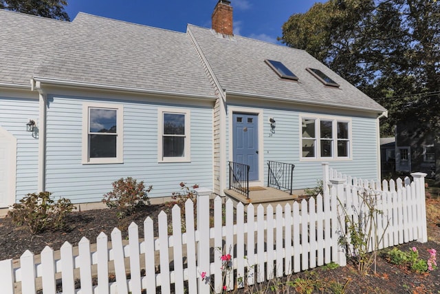 cape cod-style house with roof with shingles, a fenced front yard, and a chimney