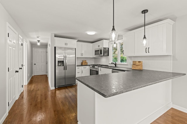 kitchen with white cabinets, dark countertops, appliances with stainless steel finishes, decorative light fixtures, and a peninsula