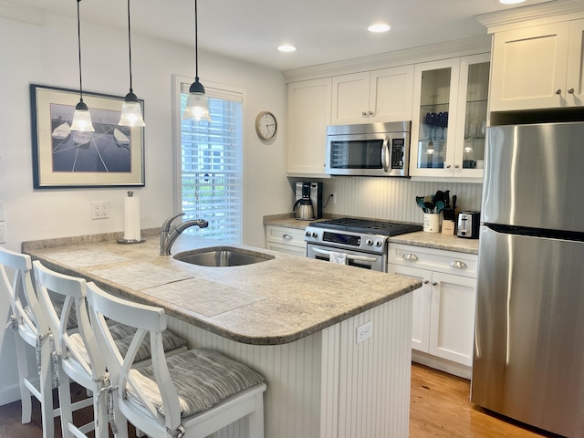 25 Milestone Way, Mashpee, MA 02649 - kitchen with stainless steel appliances, a sink, glass insert cabinets, a breakfast bar, and light wood-type flooring