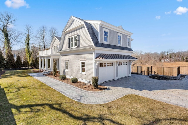 view of side of property featuring decorative driveway, a shingled roof, a lawn, a gambrel roof, and fence