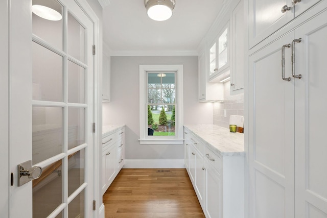 44 Tonset Rd, Orleans, MA 02653 - kitchen with glass insert cabinets, white cabinets, light wood-type flooring, crown molding, and backsplash