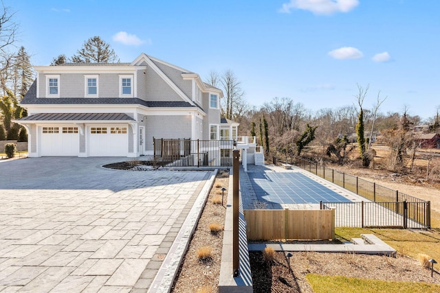 view of home's exterior with roof with shingles, an attached garage, fence, a deck, and decorative driveway