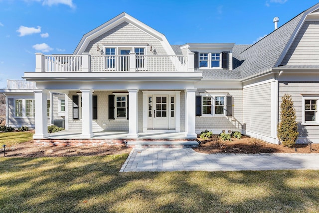 shingle-style home featuring a balcony, covered porch, a gambrel roof, roof with shingles, and a front lawn