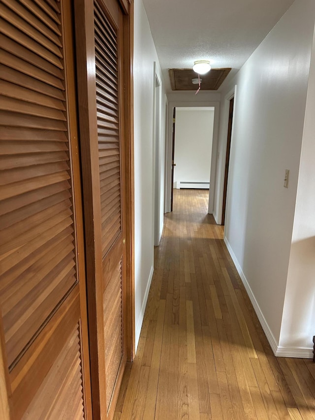 hallway with a baseboard heating unit, hardwood / wood-style flooring, and baseboards