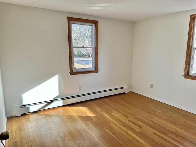 unfurnished room with light wood-style floors, a baseboard heating unit, and baseboards