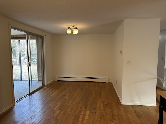 spare room with baseboards, wood-type flooring, a baseboard heating unit, and a notable chandelier